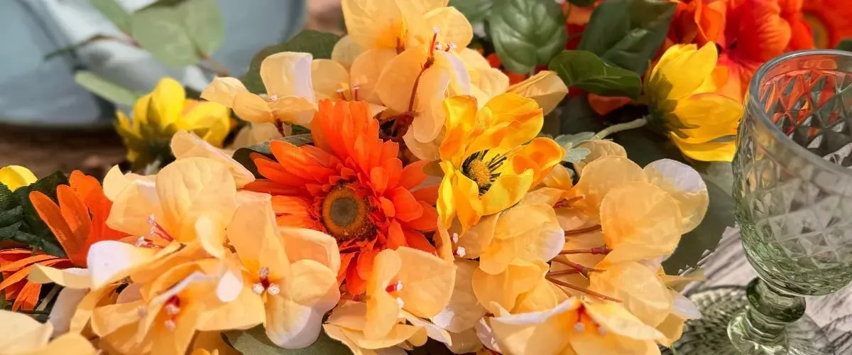 Oranje en gele bloemen naast een groen geslepen glas op een gedekte tafel
