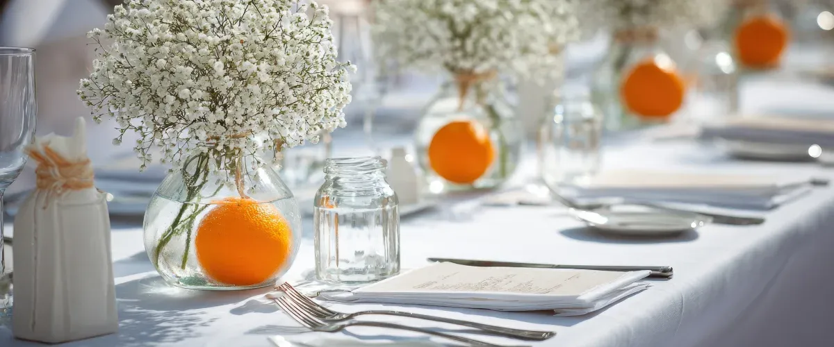 Lange witte tafel met gipskruid in glazen vazen en sinaasappels als accent