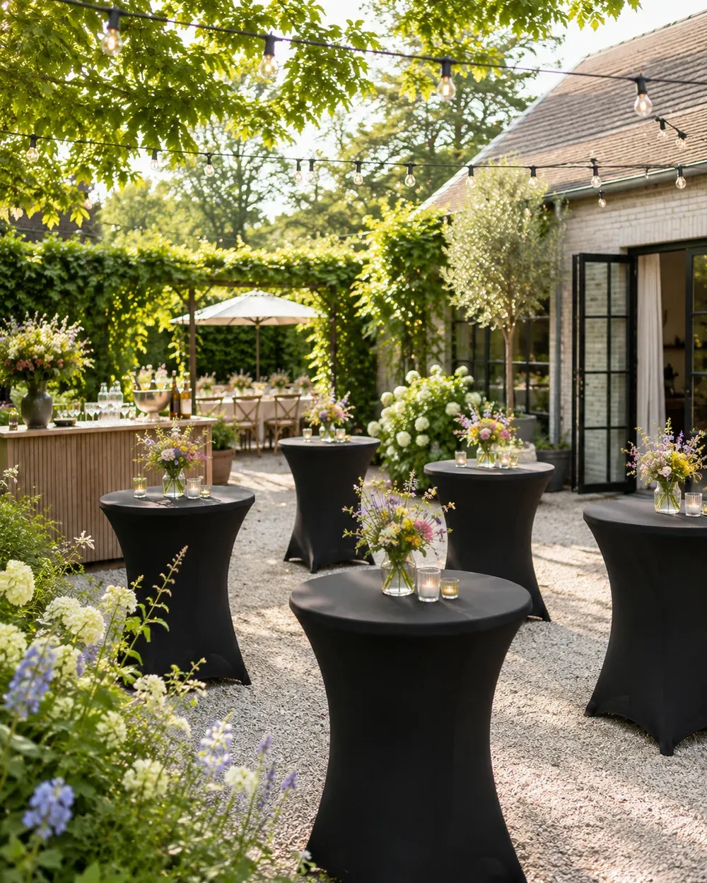Statafels met veldbloemen en lichtsnoeren op een tuinfeest